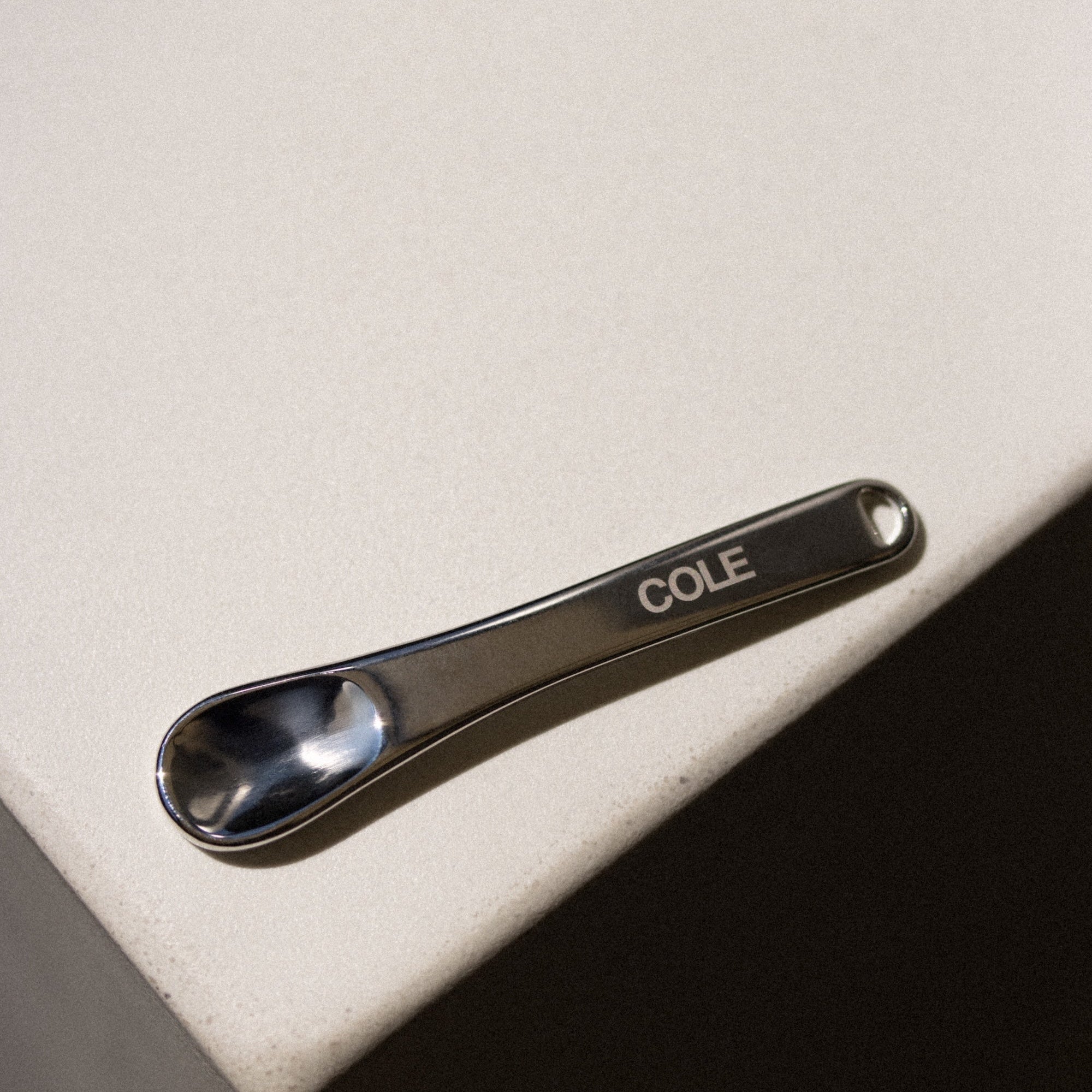 Metallic spoon with 'COLE' engraving on a beige surface