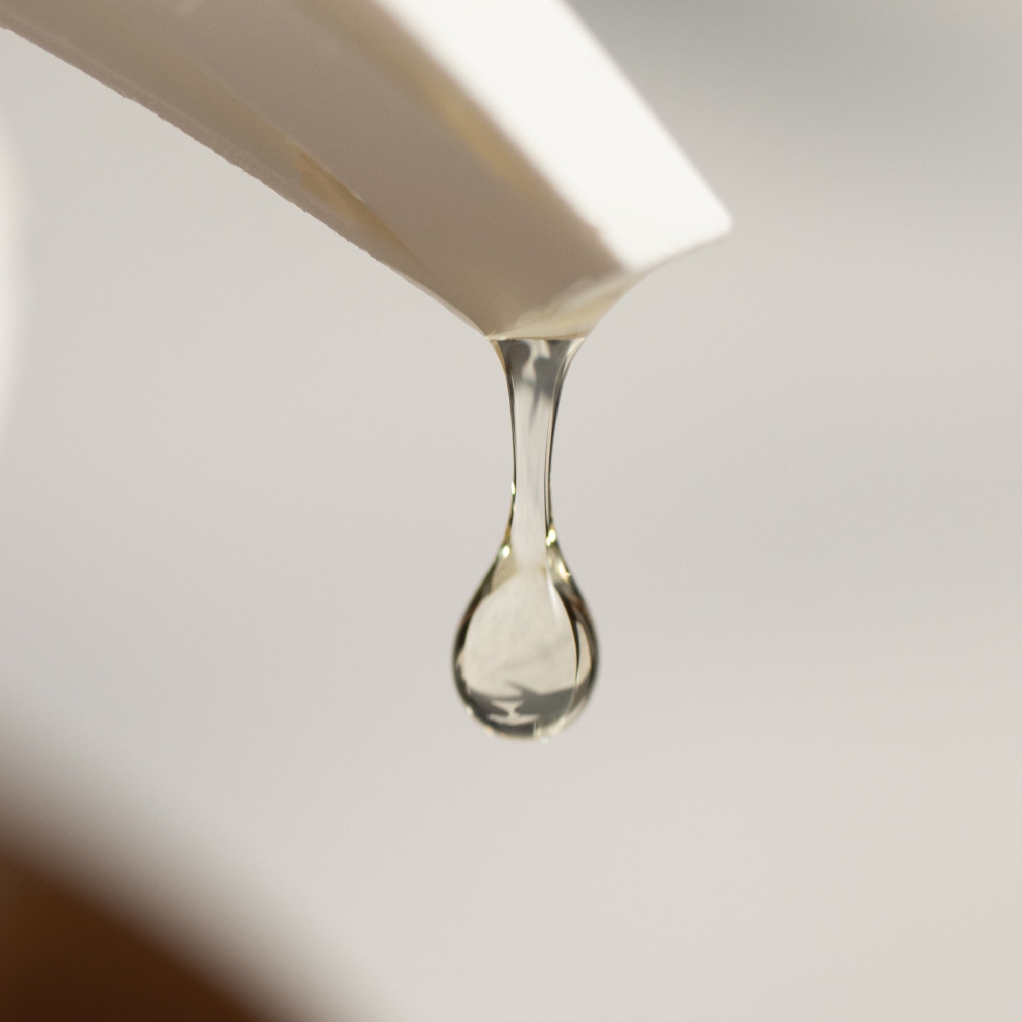Close-up of a dropper with liquid being dripped onto a light surface.