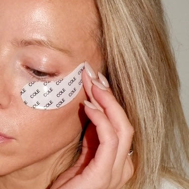 Person applying eye patches with 'Cole' branding to their eyes.
