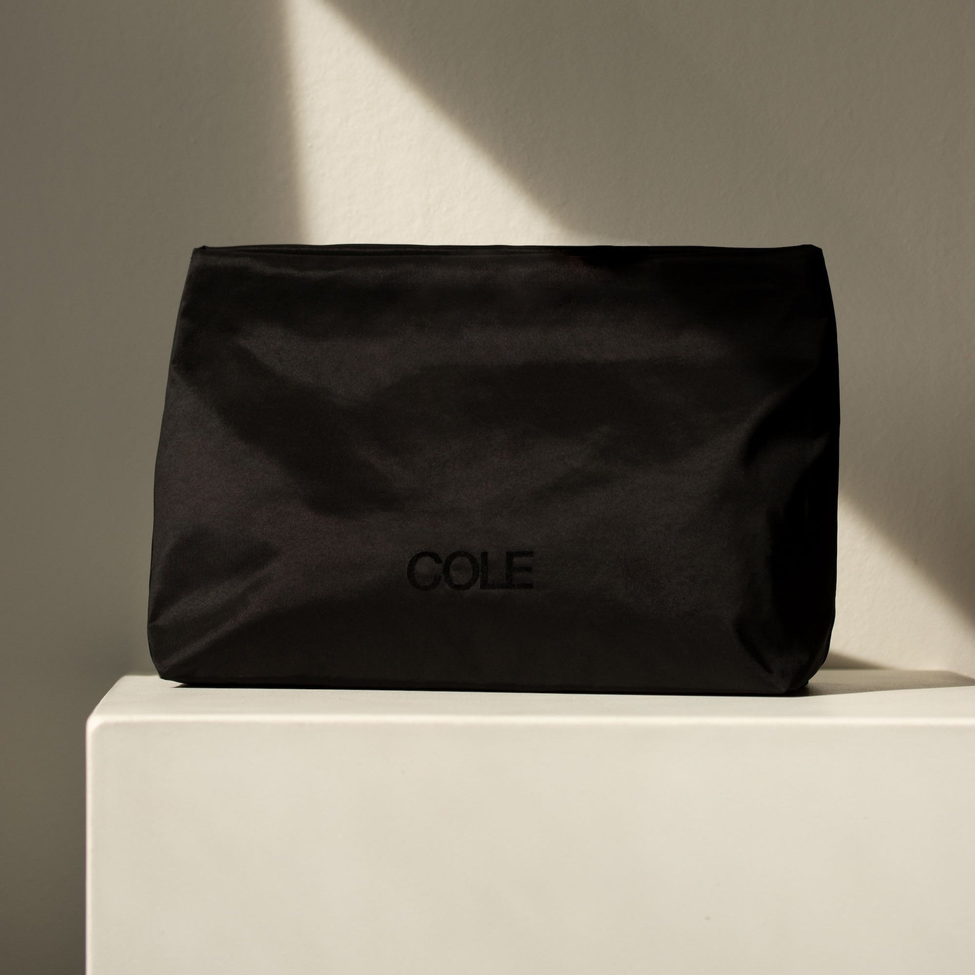 Black pouch with 'COLE' branding on a beige surface and gray background