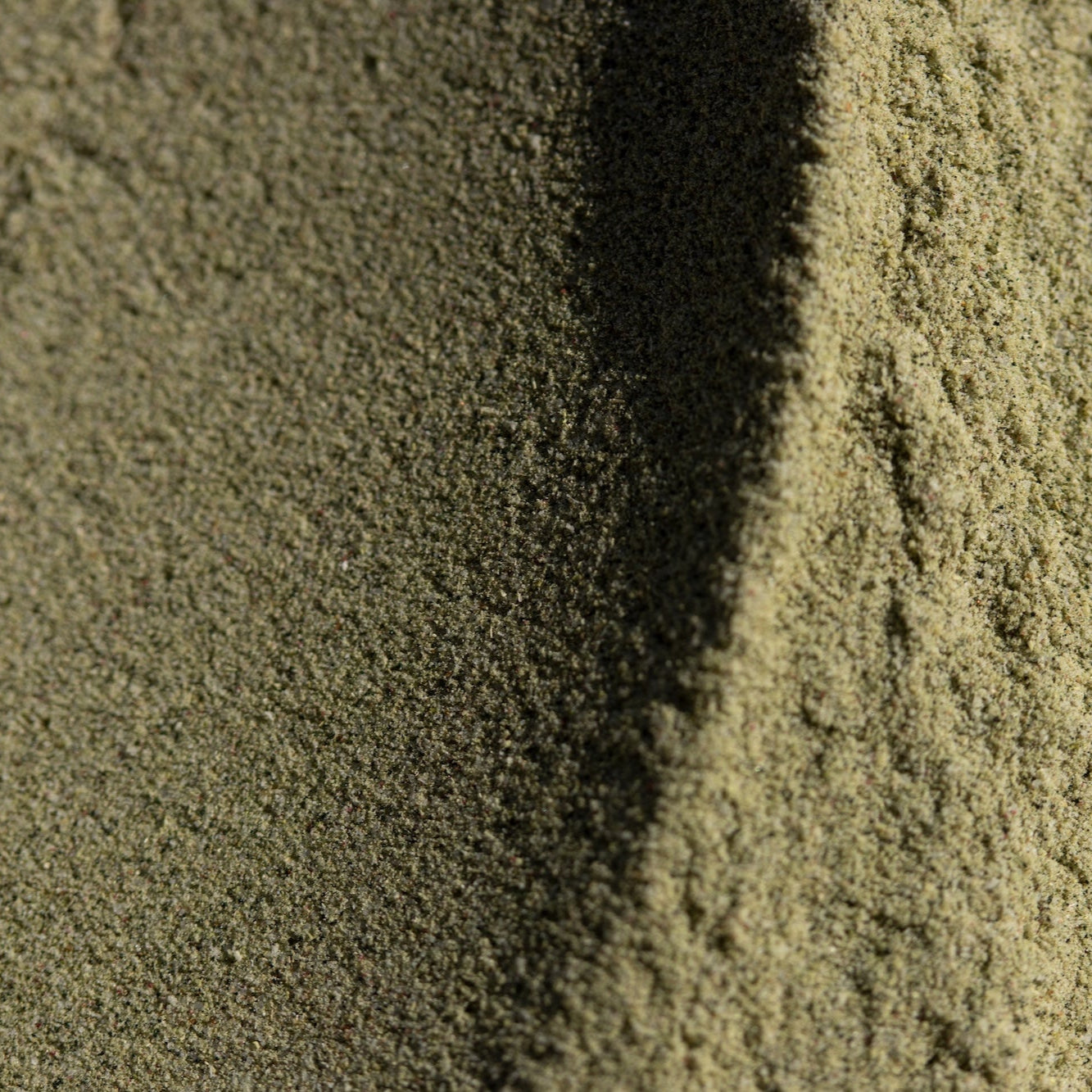 Close-up of green powder with a shadow on a textured surface